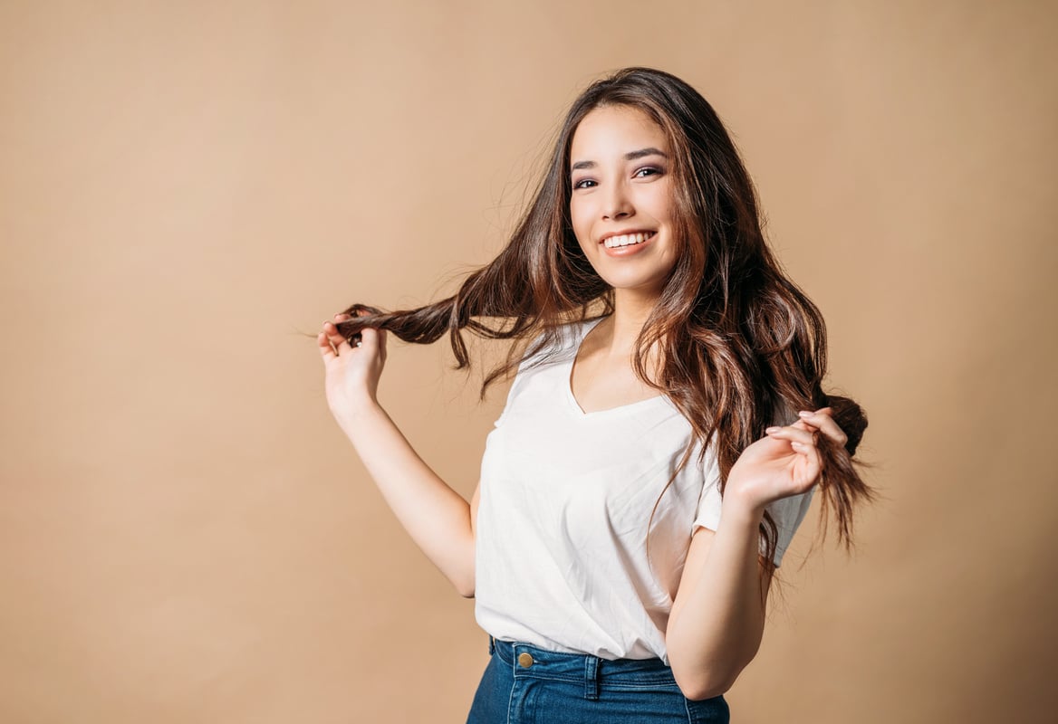 Young Woman Playing with Hair on Beige Background