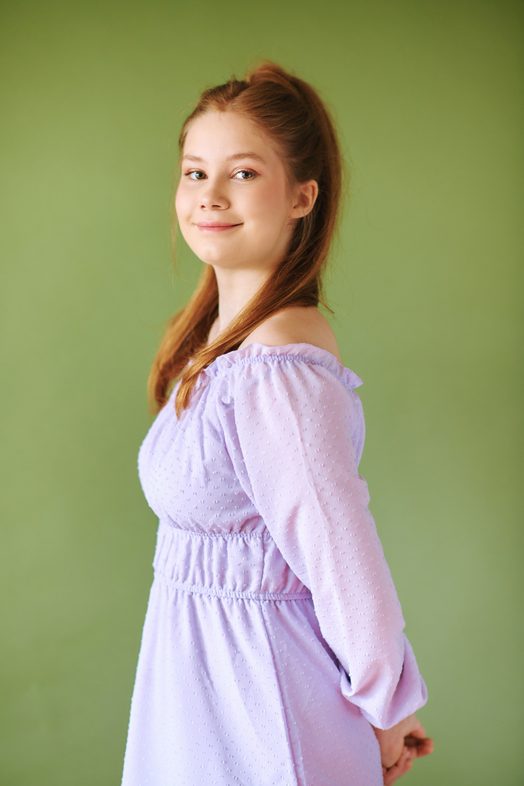 Beauty portrait of pretty young 15 - 16 year old redhaired teeenage girl wearing purple dress posing on green background