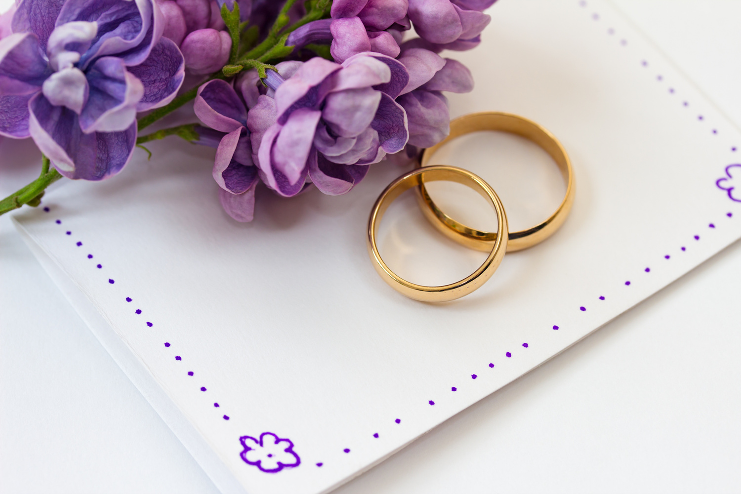 Wedding rings, invitation and flowers of lilac.